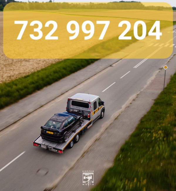 Widok z lotu ptaka na lawetę pomocy drogowej ze Słupska, jadącą tyłem do kamery w stronę skrzyżowania. Po lewej stronie widać pola, a na górnym żółtym pasku widnieje biały numer telefonu